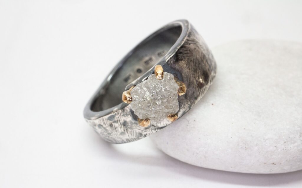 Hangdjorda smycken i silver. En bild på en handgjord ring med en oslipad diamant. Ringen är gjord av oxiderat sterling silver, stenfattningen är gjord av 9K guld.